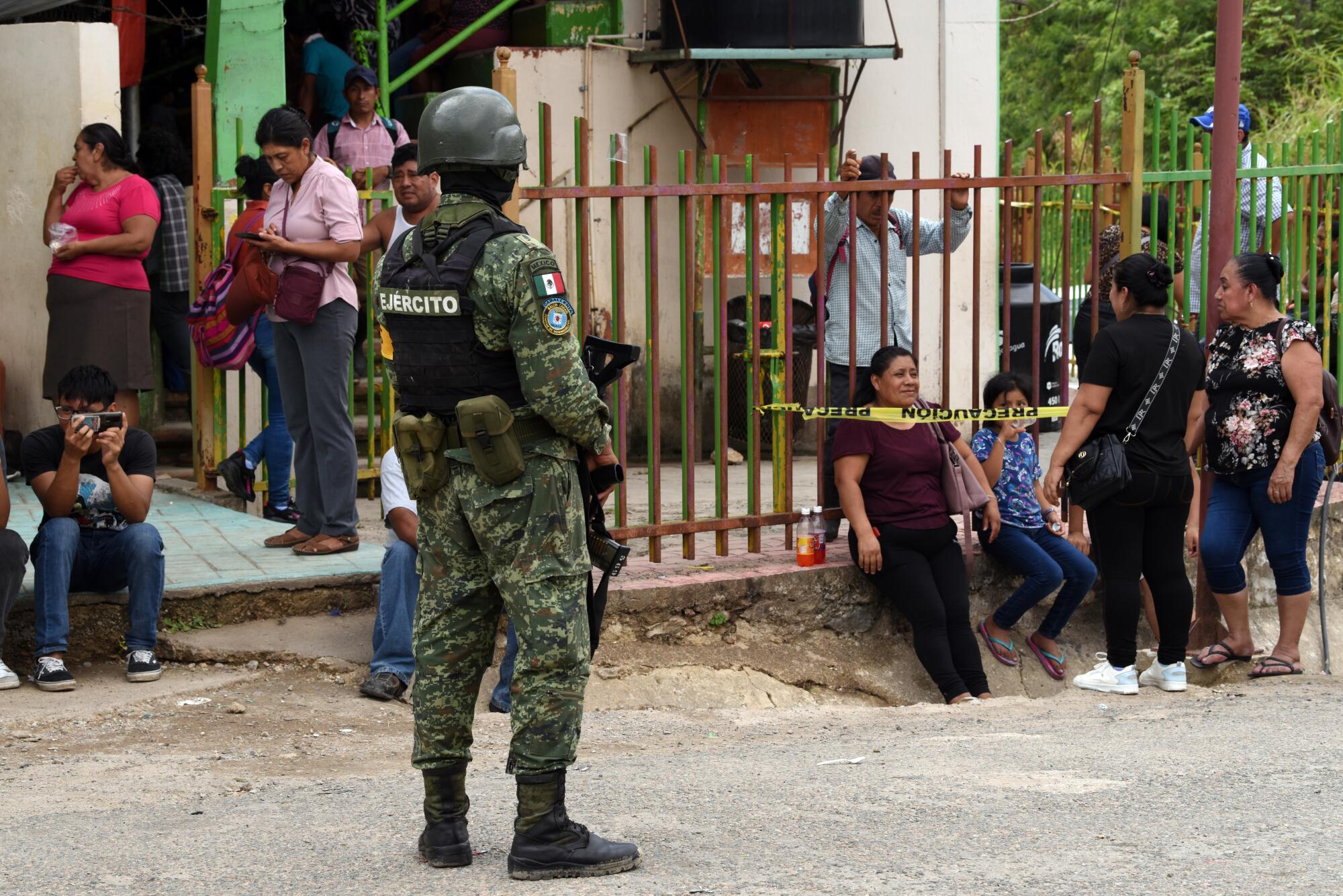 A soldier in uniform stands near people milling about a building