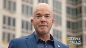 An image of a man with light-toned skin and a bald head, wearing a suit.